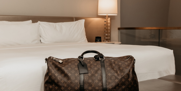 A hotel room bed with a Louis Vuitton bag in the foreground.