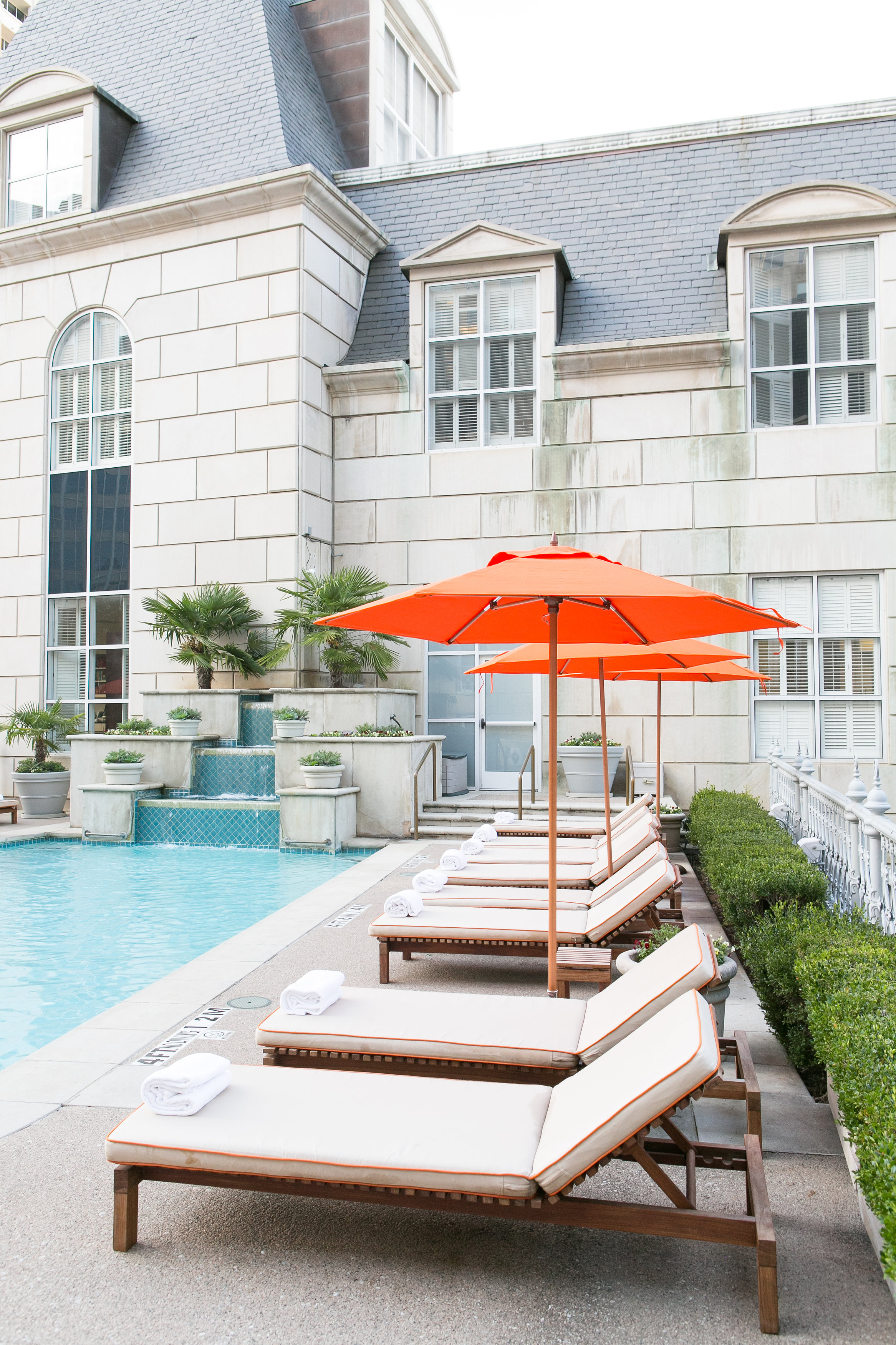 A poolside area with lounge chairs, umbrellas, and a fountain in the background.